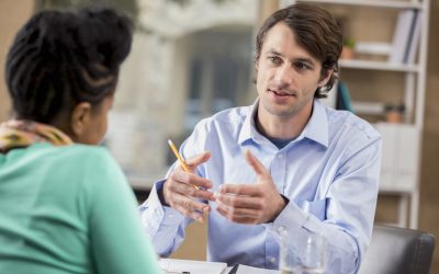 Confident mid adult Caucasian manager interviews prospective African American female employee. The man is gesturing while talking. The woman's back is to the camera.